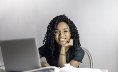 Happy ethnic woman sitting at table with laptop