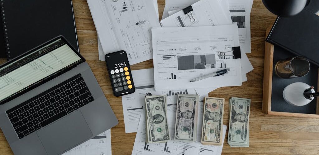 A Laptop Near the Dollars and Papers on a Wooden Table